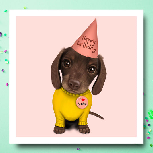 Birthday card with Dachshund Puppy wearing a Yellow Jumper, "I love Cake" Badge and party hat 