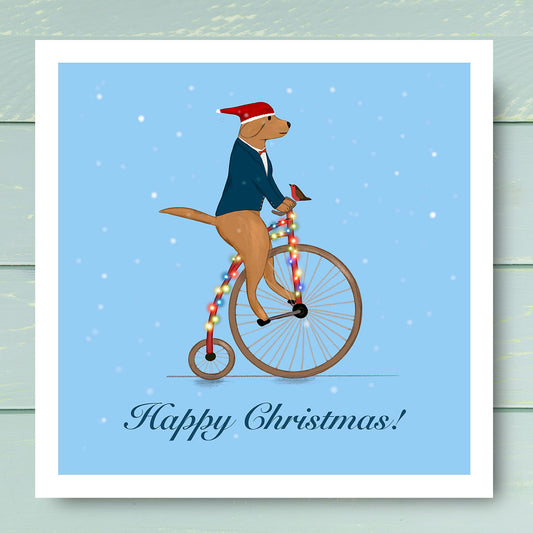 Labrador riding Unicycle wearing Santa hat with Robin sat on handle bars. Christmas Card illustrated by Oundle artist Kitty's Art